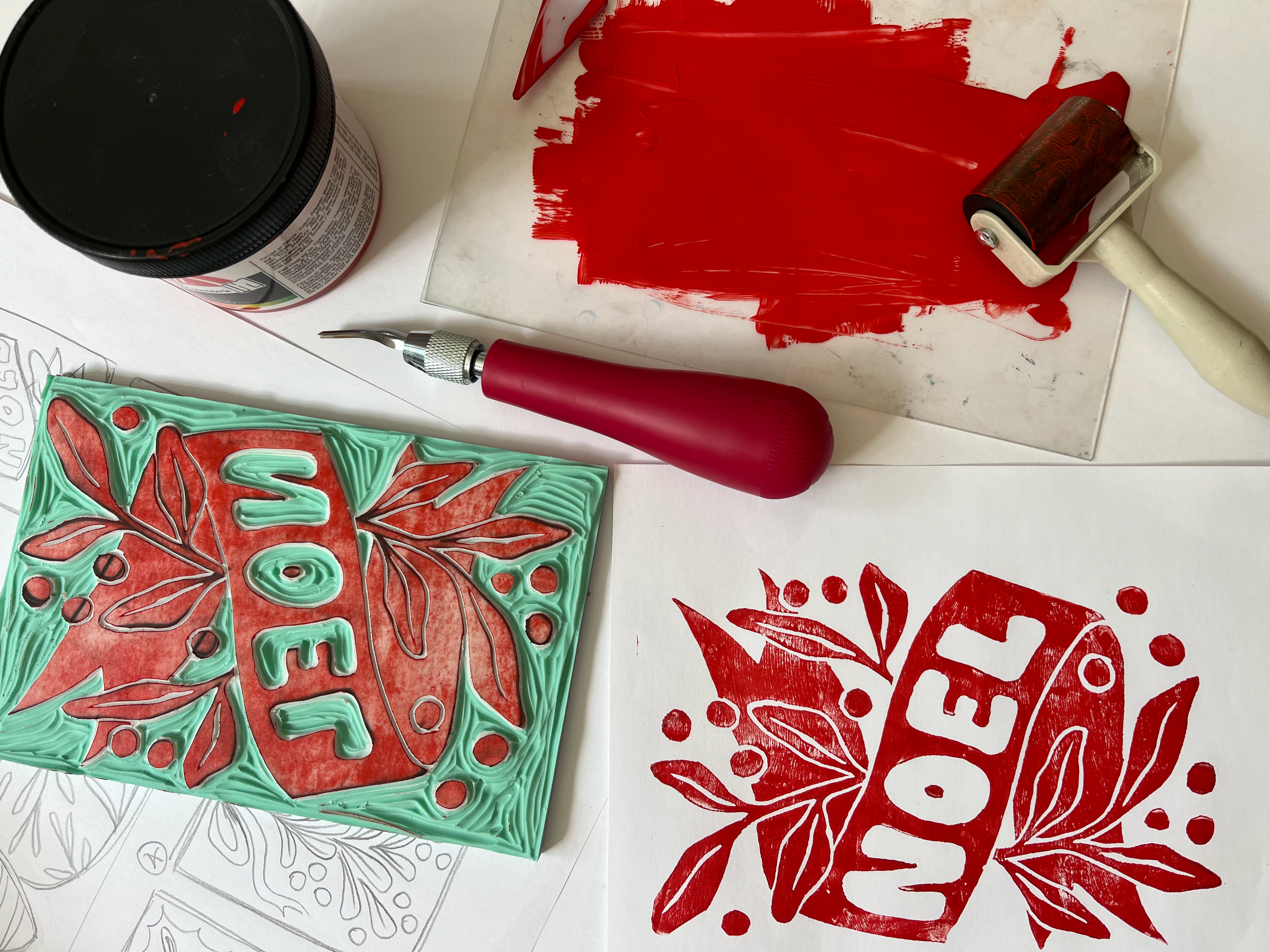 Linocut printing tools, carved block, and red holiday card design on a worktable.