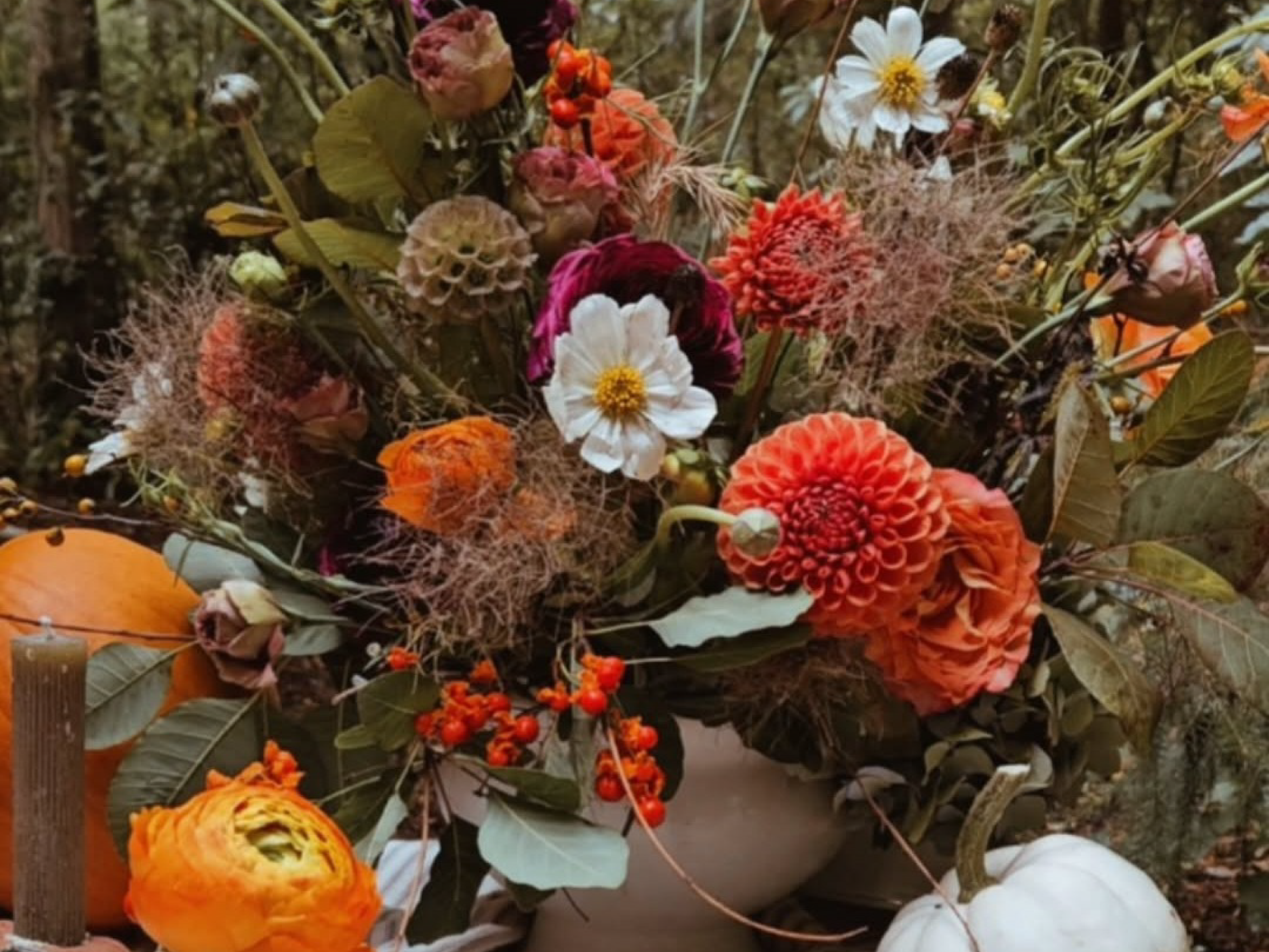 Autumn floral arrangement with orange, white, and burgundy blooms among pumpkins.