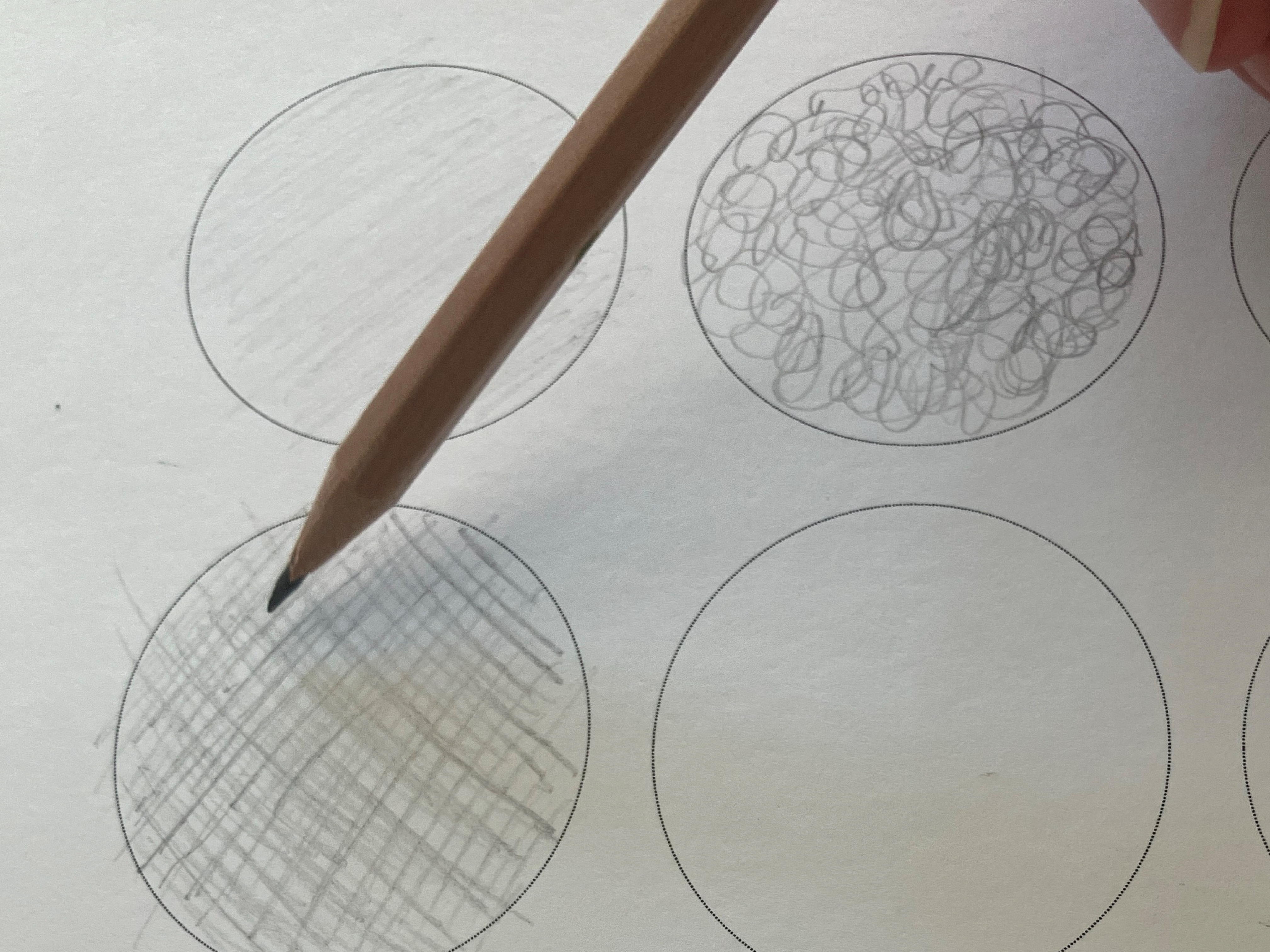 A wooden pencil using different textures to fill in circle outlines.