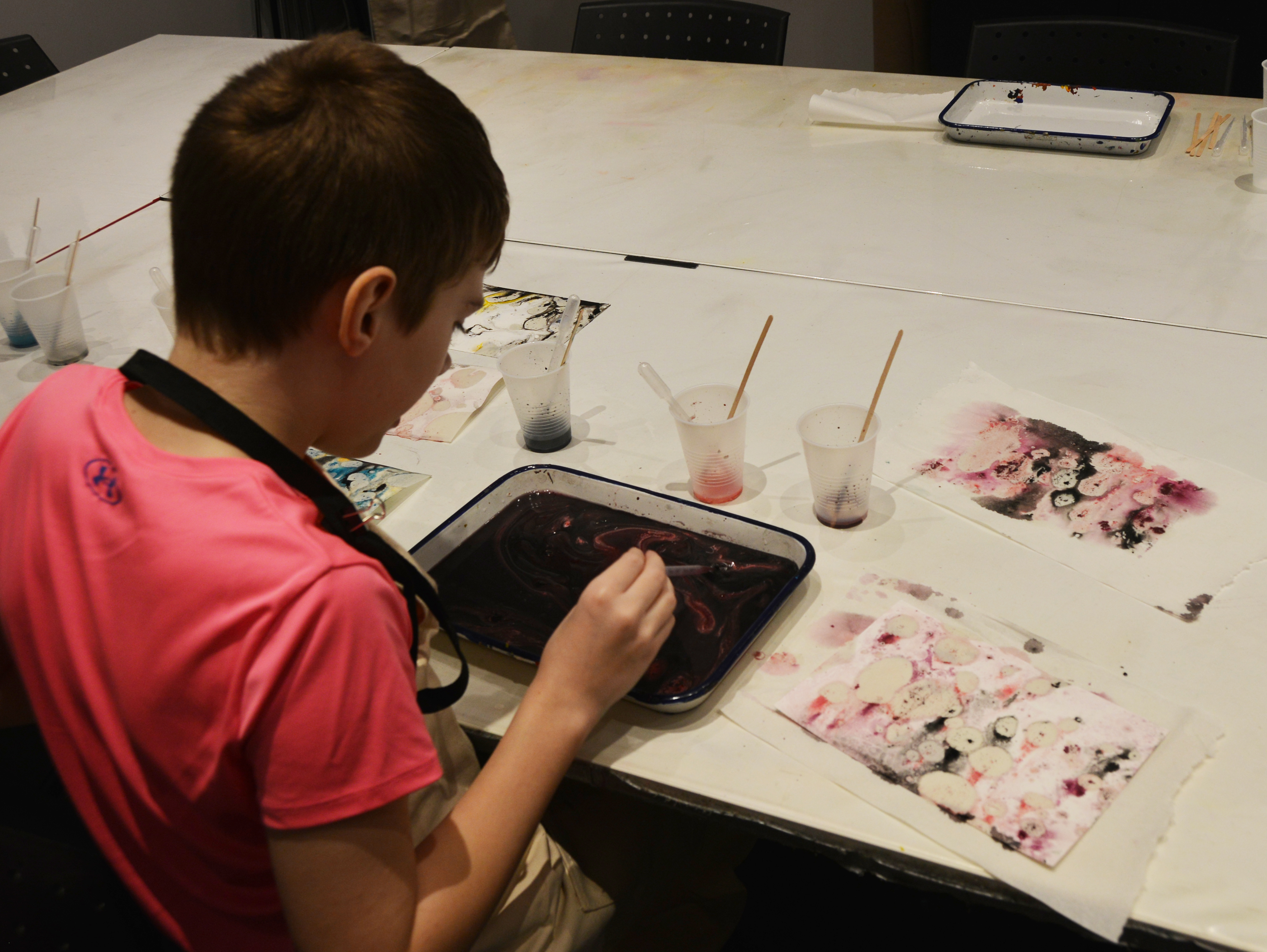 A young boy using red, purple and black dyes to create a marbled effect on paper.