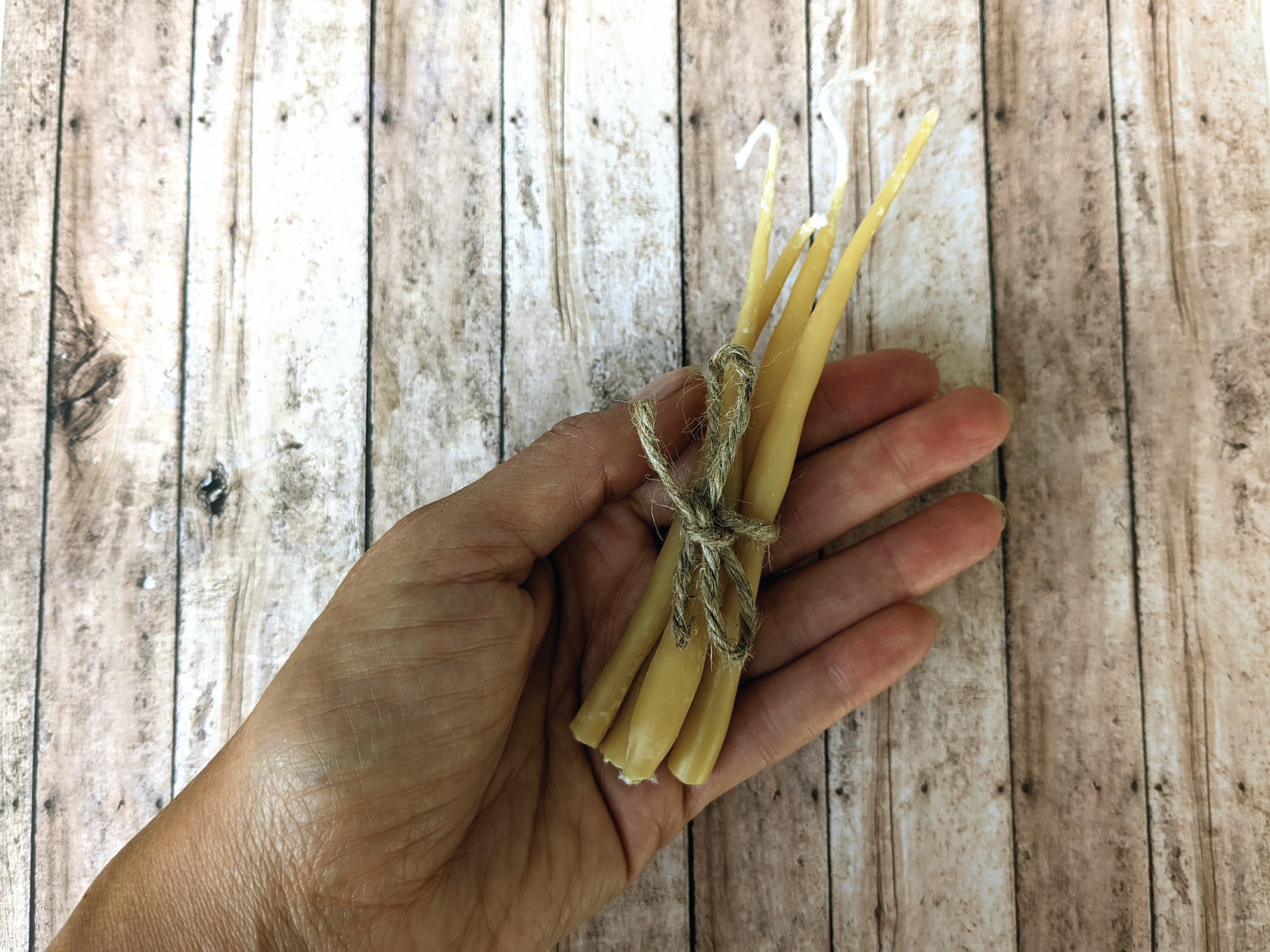 A hand holding out a small bundle of handmade candles wrapped in twine