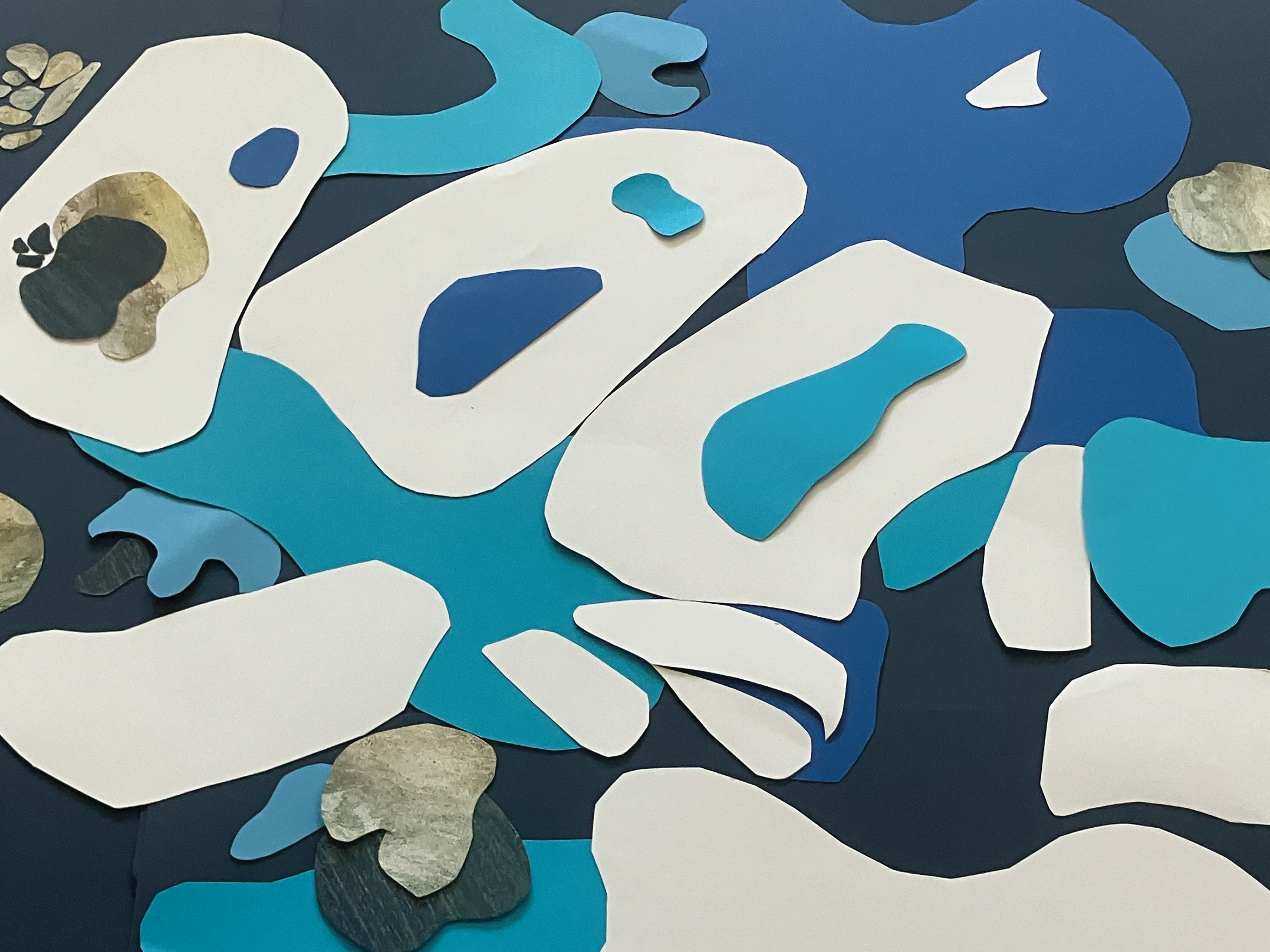 A collage of light blue, white and dark blue blobs cut from construction paper, are atop a black piece of paper, intended to mimic the look of ice flows.