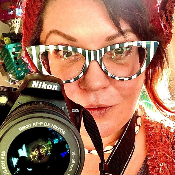 Woman with brown hair holding a camera and smiling