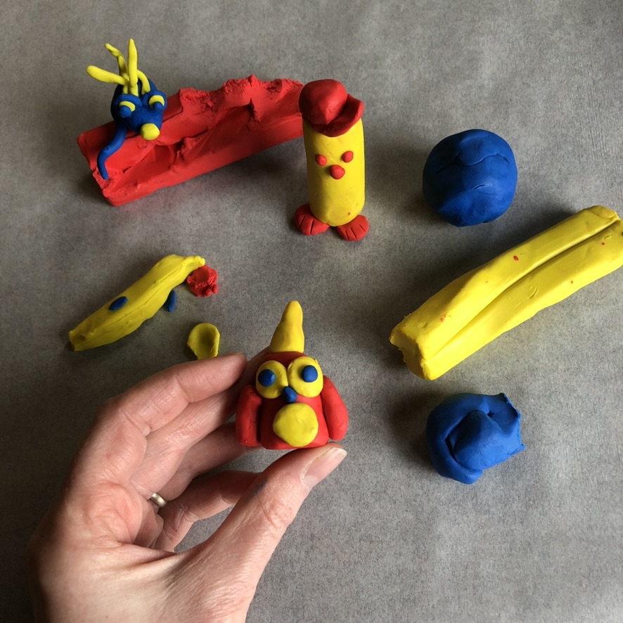 a hand holding out a clay owl crafted from red, yellow and blue clay