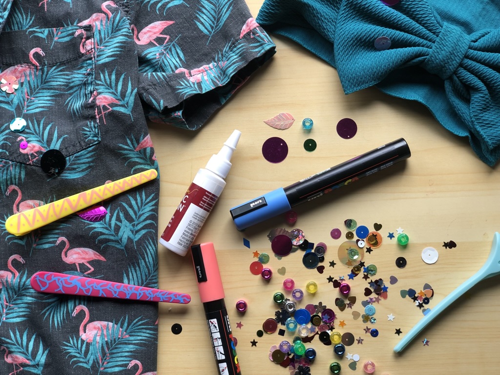 A funky button down shirt surrounded by pens, sequins, beads and glue.